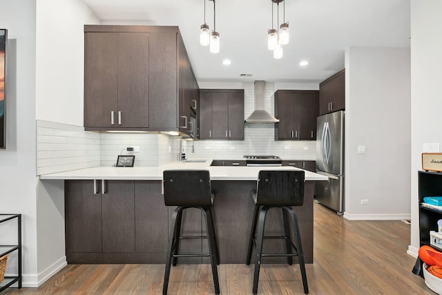 kitchen with wall chimney range hood, appliances with stainless steel finishes, dark brown cabinets, a peninsula, and dark wood-type flooring