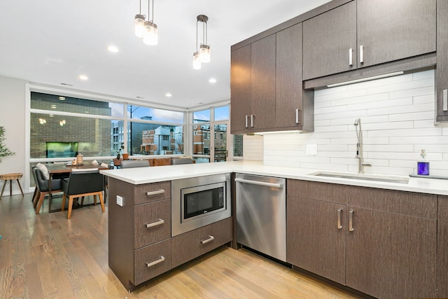 kitchen with a sink, light countertops, stainless steel appliances, decorative backsplash, and light wood-type flooring