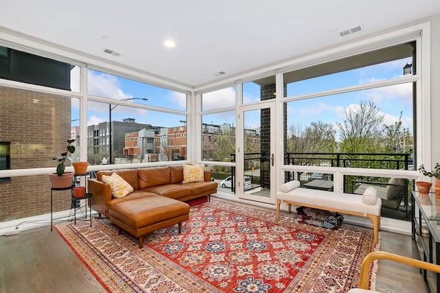 sunroom with brick wall, visible vents, floor to ceiling windows, and wood finished floors