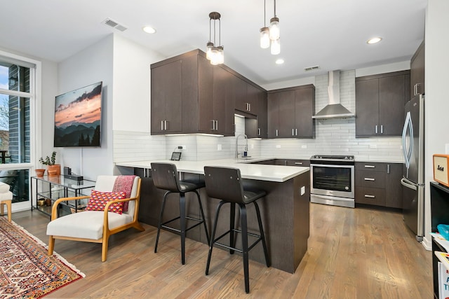 kitchen with visible vents, a peninsula, wall chimney exhaust hood, a sink, and stainless steel appliances