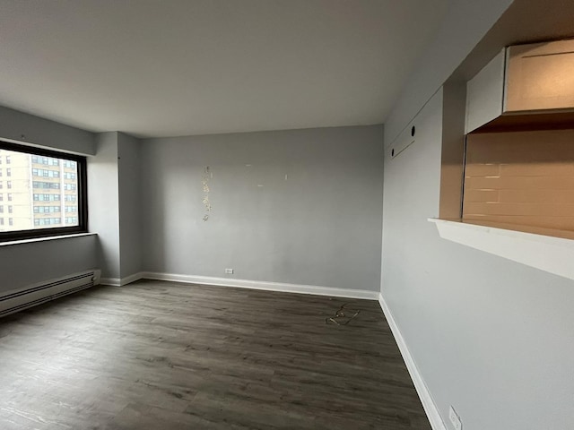 spare room featuring baseboards, a baseboard heating unit, and dark wood-style floors
