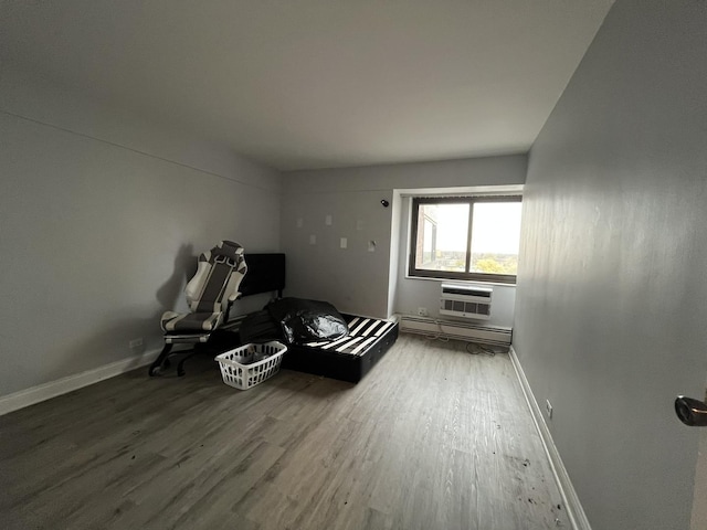 bedroom featuring an AC wall unit, baseboards, baseboard heating, and wood finished floors