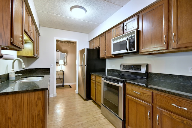 kitchen with a sink, baseboards, light wood finished floors, dark stone counters, and stainless steel appliances