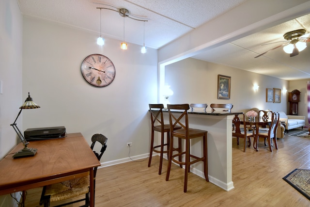 dining room featuring baseboards, ceiling fan, light wood-type flooring, and a textured ceiling