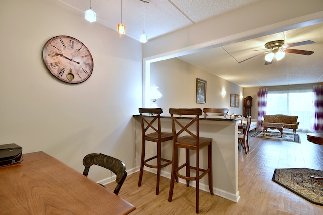 kitchen featuring baseboards, a kitchen breakfast bar, ceiling fan, and wood finished floors