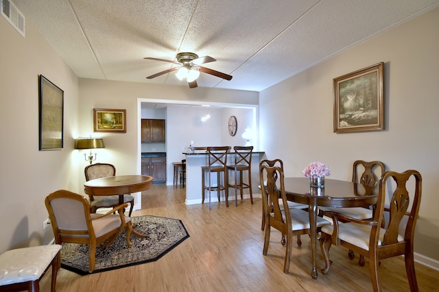 dining space featuring light wood-style floors, a ceiling fan, a textured ceiling, and visible vents