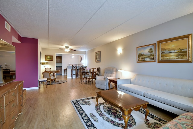 living room with a ceiling fan, a textured ceiling, visible vents, and wood finished floors