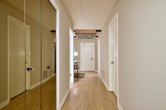 corridor featuring visible vents, baseboards, a chandelier, and light wood finished floors