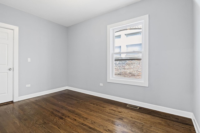 unfurnished room with baseboards, visible vents, and dark wood-type flooring