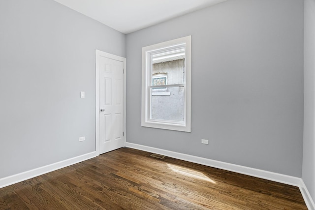 empty room with baseboards, visible vents, and dark wood-style floors