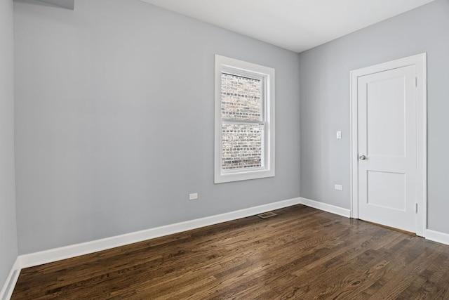 spare room featuring baseboards, dark wood-style flooring, and visible vents