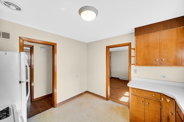 kitchen featuring visible vents, freestanding refrigerator, light countertops, brown cabinets, and range