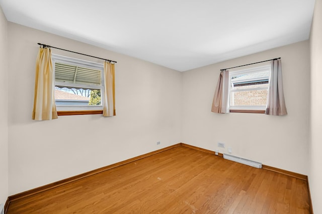 unfurnished room with baseboards, a wealth of natural light, light wood-style floors, and a baseboard radiator
