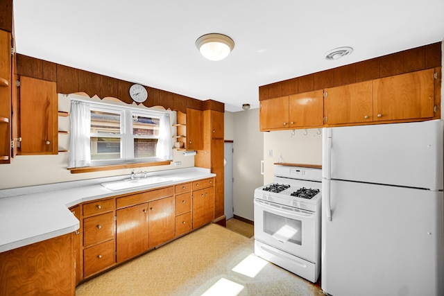 kitchen featuring brown cabinetry, a sink, white appliances, and light countertops