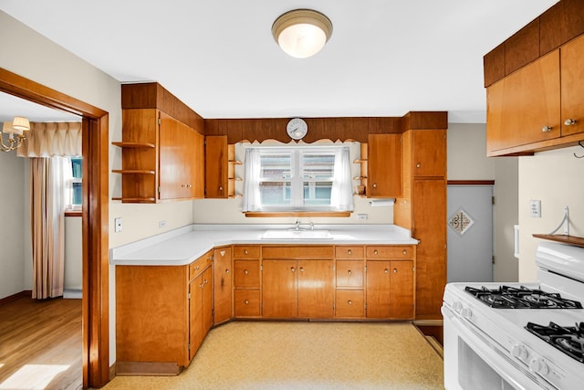 kitchen featuring brown cabinetry, open shelves, a sink, light countertops, and white range with gas stovetop