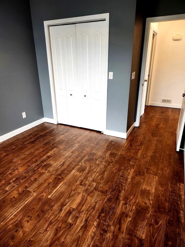 unfurnished bedroom with baseboards, a closet, dark wood-style floors, and visible vents