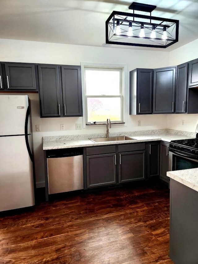 kitchen with black gas range oven, a sink, dishwasher, freestanding refrigerator, and dark wood-type flooring
