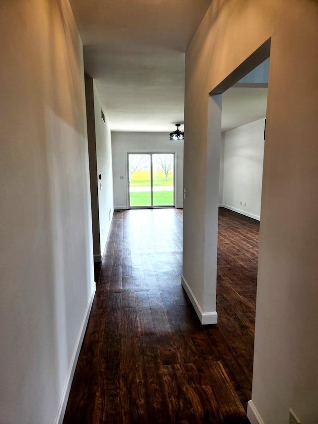 corridor featuring baseboards, dark wood-style flooring, and a notable chandelier