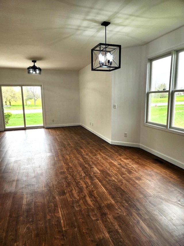 unfurnished dining area featuring dark wood-style flooring, a notable chandelier, and a healthy amount of sunlight