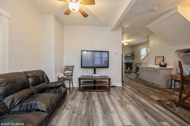 living area with a ceiling fan, beam ceiling, wood finished floors, baseboards, and stairs