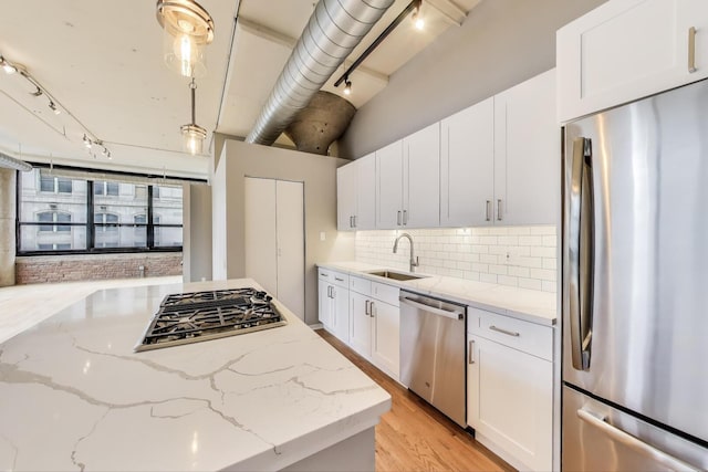 kitchen featuring tasteful backsplash, a sink, track lighting, stainless steel appliances, and white cabinetry