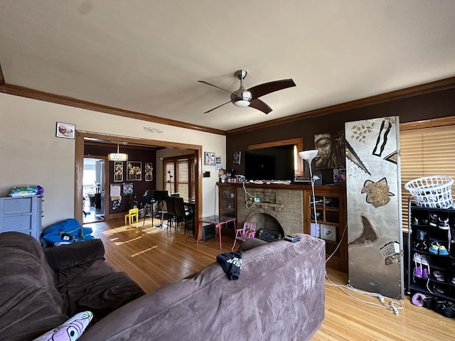 living room with a brick fireplace, a ceiling fan, ornamental molding, and wood finished floors