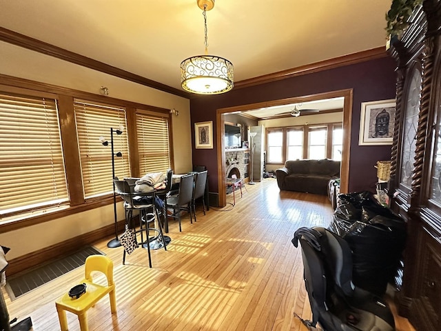living area with baseboards, ornamental molding, a stone fireplace, and light wood-type flooring
