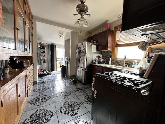 kitchen featuring a sink, tile patterned flooring, freestanding refrigerator, black gas stove, and backsplash