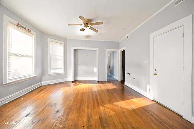 spare room featuring wood-type flooring, a ceiling fan, baseboards, visible vents, and ornamental molding