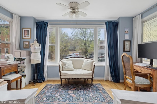 living area with baseboards, ornamental molding, a ceiling fan, and wood finished floors