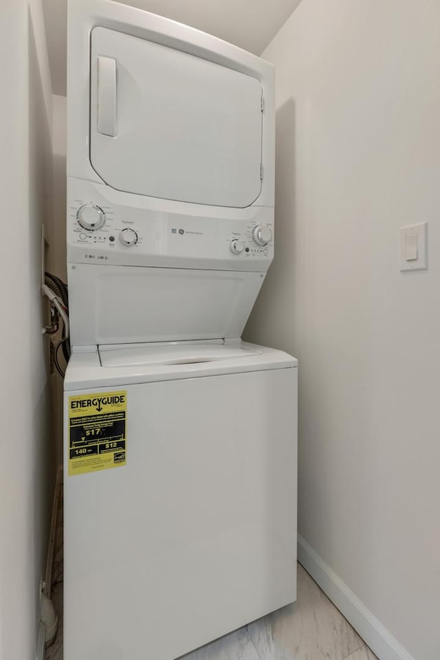 laundry room with baseboards, laundry area, stacked washer / dryer, and marble finish floor