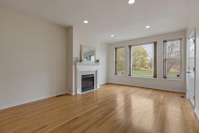 unfurnished living room featuring light wood finished floors, recessed lighting, baseboards, a fireplace with flush hearth, and visible vents