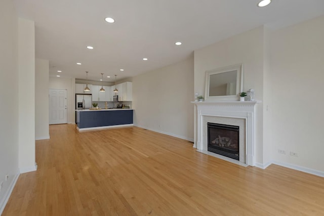 unfurnished living room featuring recessed lighting, a fireplace with flush hearth, light wood-style flooring, and baseboards