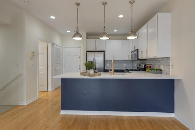 kitchen featuring backsplash, appliances with stainless steel finishes, a sink, baseboards, and a peninsula