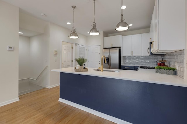 kitchen with backsplash, decorative light fixtures, appliances with stainless steel finishes, a sink, and a peninsula