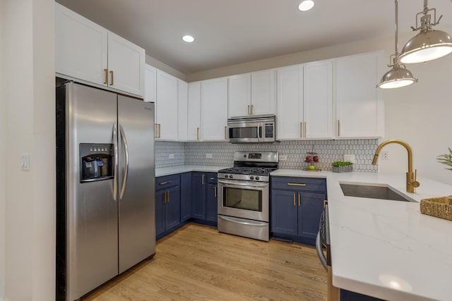 kitchen with appliances with stainless steel finishes, a sink, blue cabinetry, white cabinetry, and tasteful backsplash
