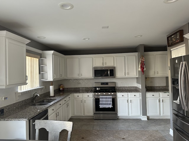 kitchen featuring appliances with stainless steel finishes, a sink, dark stone counters, white cabinetry, and tasteful backsplash