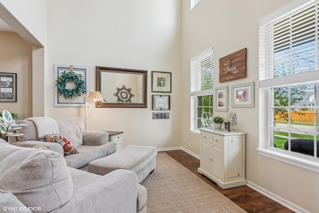 living area with plenty of natural light, dark wood-style floors, baseboards, and a high ceiling