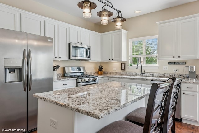 kitchen featuring appliances with stainless steel finishes, white cabinets, light stone counters, a kitchen bar, and recessed lighting