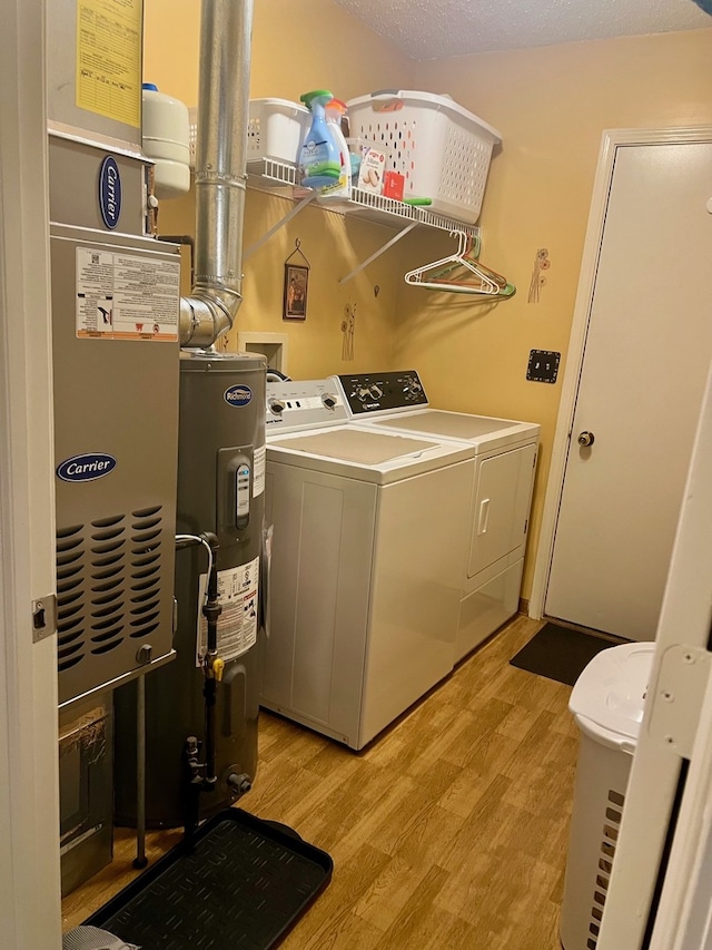 washroom featuring water heater, light wood-style floors, laundry area, and washer and clothes dryer