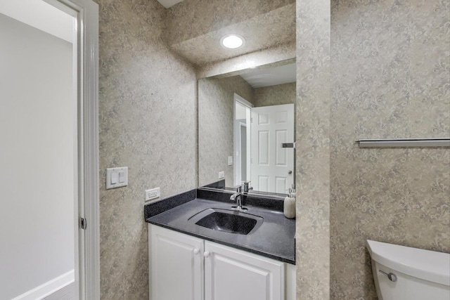 bathroom featuring toilet, vanity, and wallpapered walls