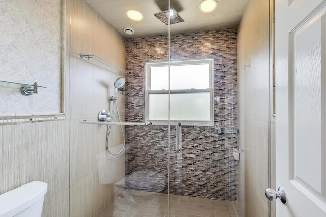 bathroom featuring a stall shower, toilet, and tile walls