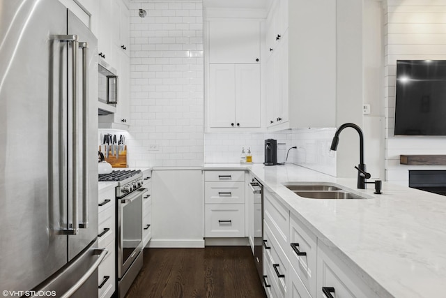 kitchen featuring appliances with stainless steel finishes, light stone countertops, dark wood finished floors, a sink, and white cabinetry