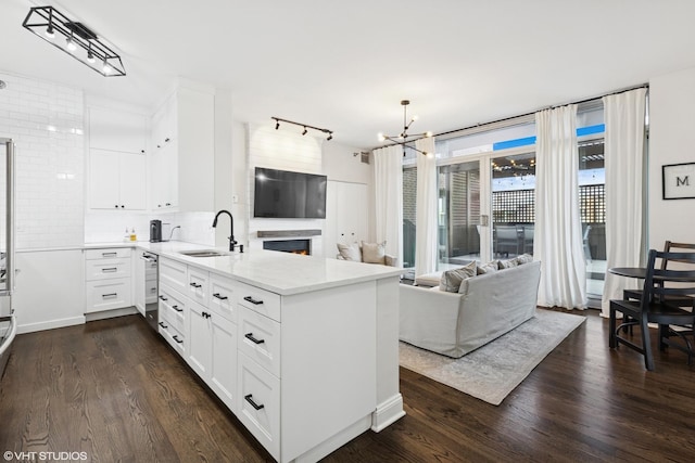 kitchen featuring dark wood-style flooring, a peninsula, open floor plan, light countertops, and a sink