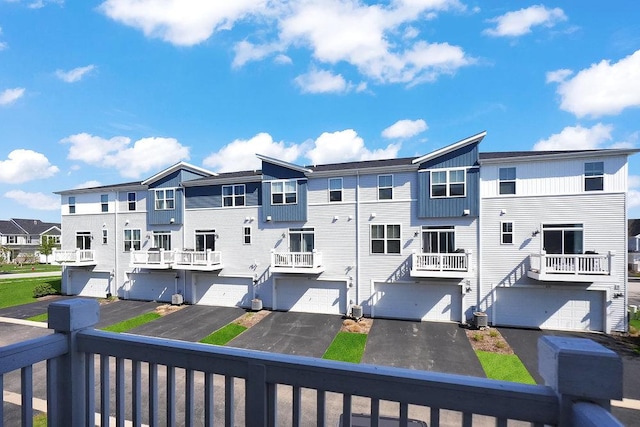 exterior space featuring an attached garage, central air condition unit, driveway, and a residential view