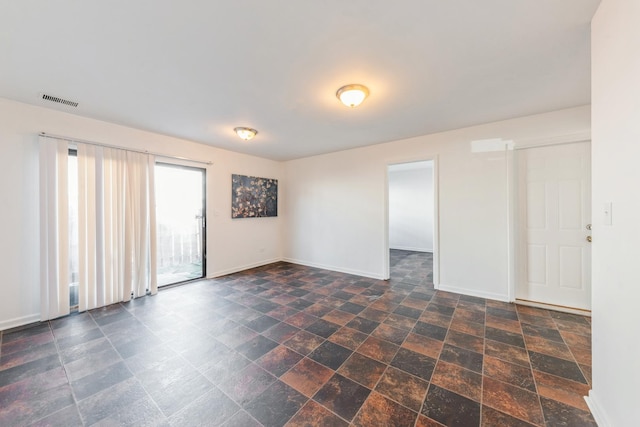empty room with baseboards, stone finish flooring, and visible vents
