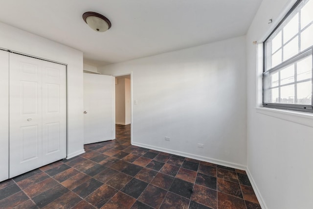 unfurnished bedroom with baseboards, a closet, and stone finish flooring