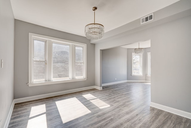 unfurnished dining area featuring visible vents, baseboards, wood finished floors, and an inviting chandelier