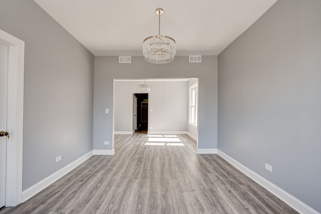 unfurnished room with visible vents, baseboards, wood finished floors, and an inviting chandelier