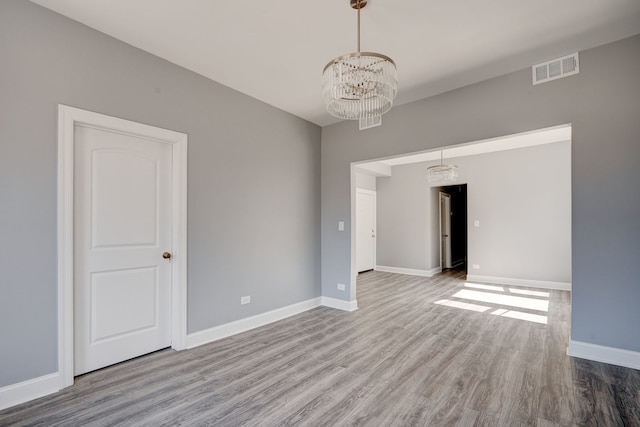 spare room with baseboards, visible vents, wood finished floors, and a notable chandelier